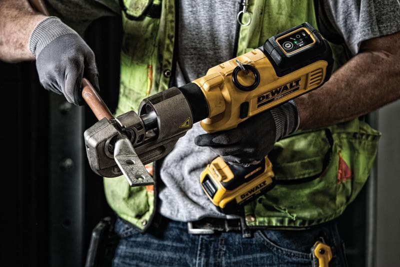 Una persona utiliza una herramienta inalámbrica DEWALT para cortar una barra de metal gruesa mientras usa guantes de trabajo y un chaleco de seguridad verde.